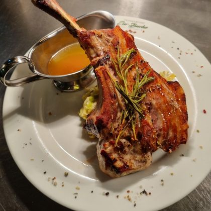 A juicy piece of meat with a bone, garnished with fresh herbs. On the side, there is a small bowl of sauce on a white plate.