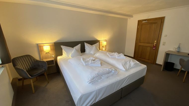A modern hotel room with a large double bed and bright walls. There is a desk and a cozy chair in the corner.