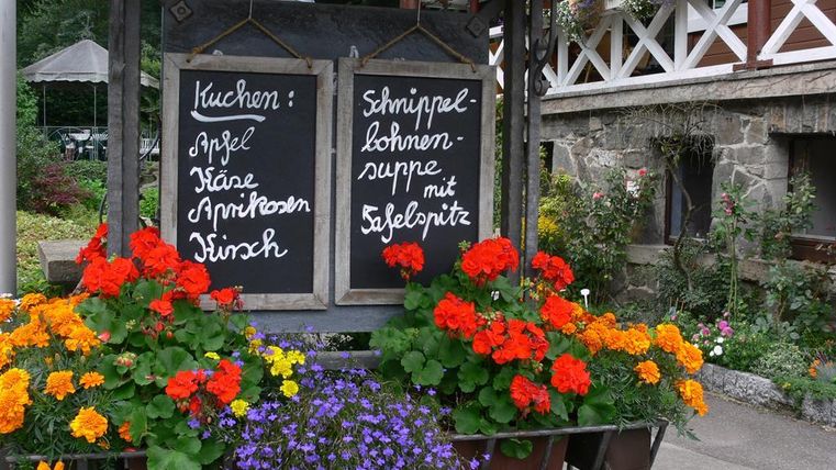 Ein Holzstand mit zwei Tafeln und bunten Blumen. Auf den Tafeln stehen Menüs mit verschiedenen Gerichten.