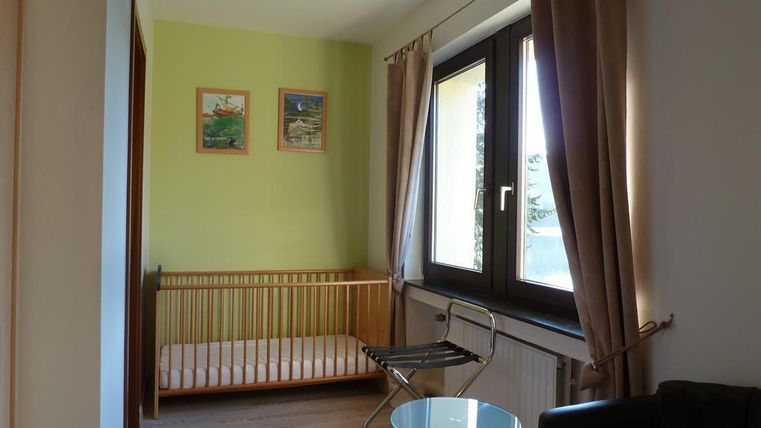 A child-friendly room with a crib and a small table. The walls are painted in soft colors and there are large windows that let in a lot of light.