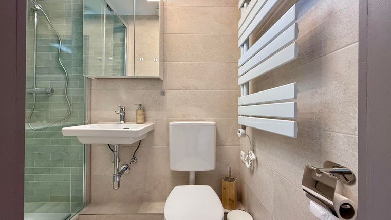 Een moderne badkamer met een douche, een wastafel en een toilet. De muren zijn licht en ontworpen met tegelsachtig materiaal.
