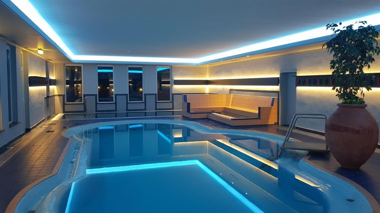 An elegant indoor swimming pool with gentle lighting. Surrounded by comfortable loungers and plants for a relaxing atmosphere.