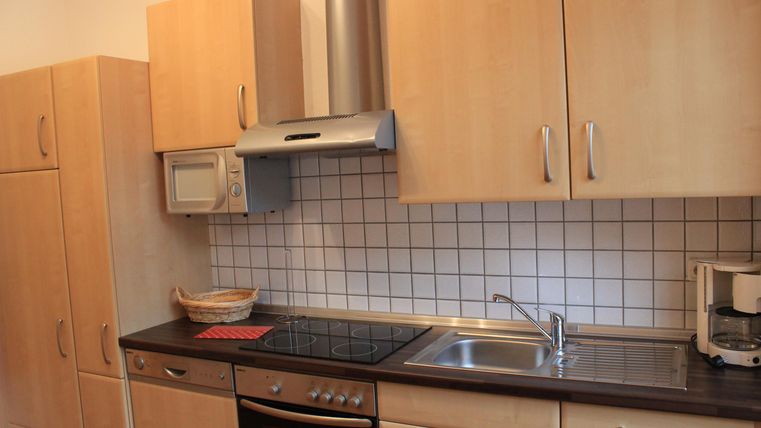 Een moderne keuken met houten kasten en een roestvrijstalen spoel. Er is een fornuis, een magnetron en een koelkast.