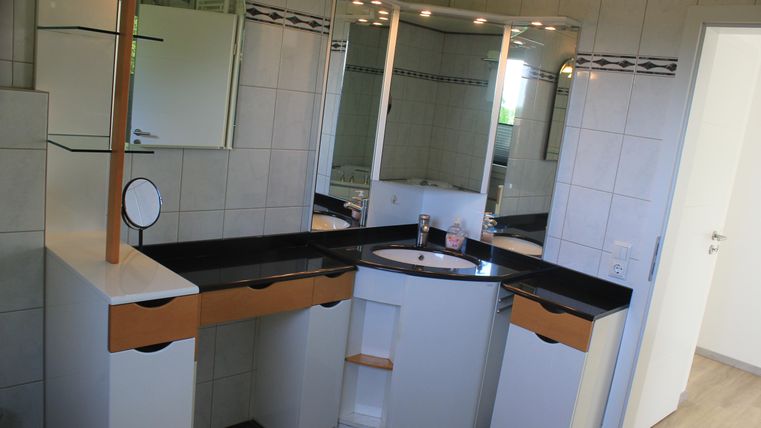 A bright bathroom with a modern sink and a large mirror. The walls are tiled, and the decor is in white and black.
