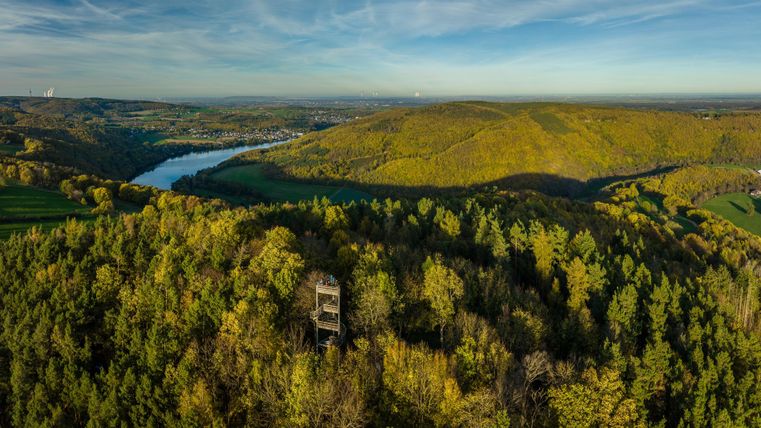Een indrukwekkend uitzicht op groene heuvels en een rivier. Tussen de bomen staat een uitkijktoren.