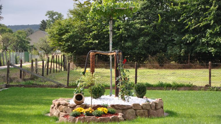 A beautiful garden with a round pile of stones and a small tree in the center. Surrounded by a green meadow and a fence.