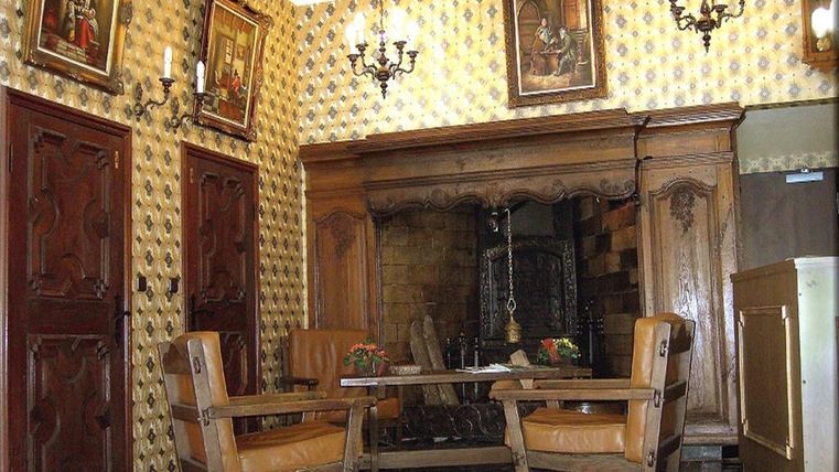 Ein gemütlicher Wohnraum mit Holzstühlen und einem Kamin. Die Wände sind mit Bildern und einer auffälligen Tapete dekoriert.