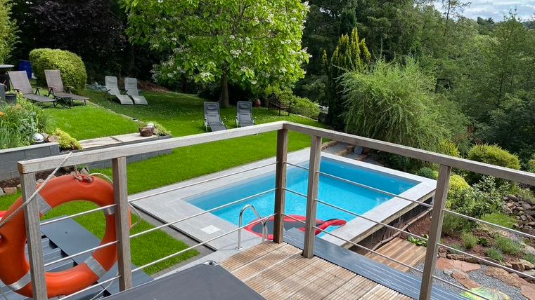 Een mooie tuin met een zwembad en groene grasvelden. Op de achtergrond staan ligstoelen onder schaduwgevende bomen.