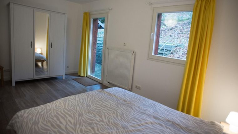 A bright bedroom with a bed and yellow curtains. The room has a wardrobe and windows overlooking a garden.