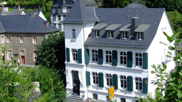 Een charmant, wit gebouw met groene luiken. Omringd door bomen en andere historische gebouwen.