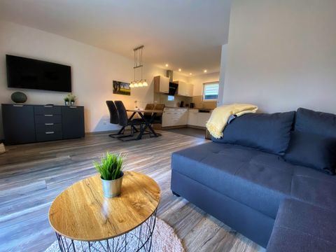 Een moderne woonkamer met een gezellige bank en een ronde tafel. Op de achtergrond is een eetkamer met een open keuken zichtbaar.