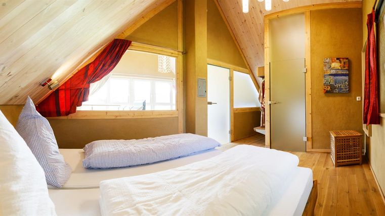A cozy bedroom in the attic with wooden paneling and two beds. Bright windows provide plenty of daylight and a welcoming atmosphere.