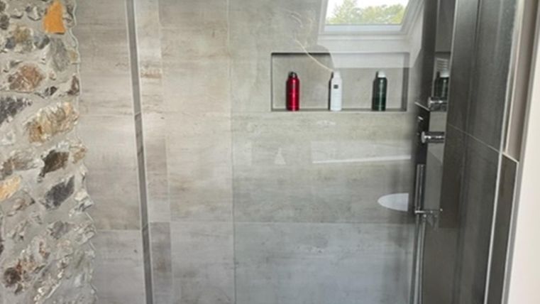 Een moderne douche met glazen scharnierdeur en elegante tegels. In de niche zijn enkele verzorgingsproducten zichtbaar.