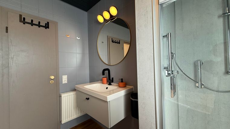 Een moderne badkamer met een wastafel en een ronde spiegel. De muren zijn in donkerblauw en grijs gehouden, en er is een douche van glas.