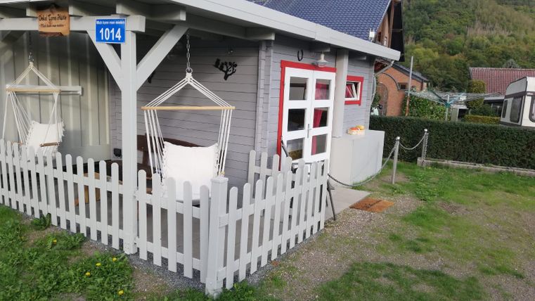 Ein gemütliches Ferienhaus mit einer Veranda und einer weißen Zaunumrandung. Die Umgebung ist grün und bietet einen Blick auf sanfte Hügel.