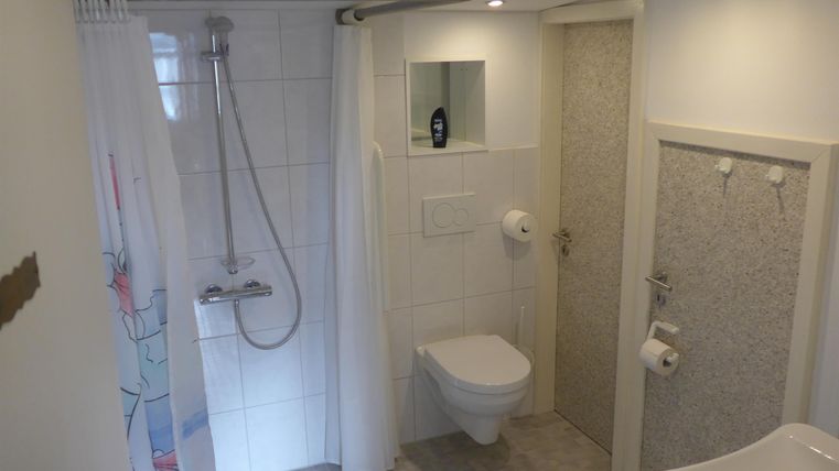 A modern bathroom with a shower, toilet, and large, bright tiles. There is a mirror and a simple, functional design.