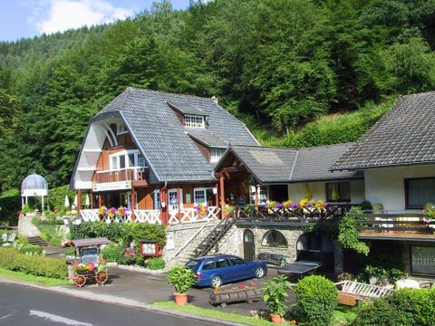 A charming house in an idyllic landscape, surrounded by trees. The garden is decorated with colorful flowers and the entrance is designed to be inviting.