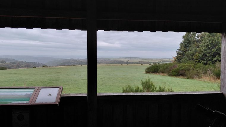 A view from a window onto a vast, green landscape with a slightly cloudy sky. In the foreground, there is an information sign.