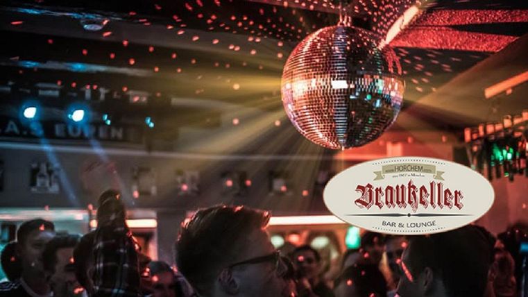 Een levendige bar met dansende mensen en een glinsterende discobal. Kleurrijke lichten creëren een feestelijke sfeer.
