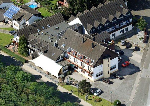 A hotel building with several floors and an adjacent parking lot. Surrounded by trees and a quiet neighborhood.