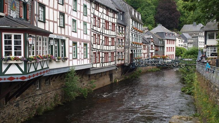 A picturesque town view with half-timbered houses along a tranquil river. The green landscape in the background complements the charming atmosphere.