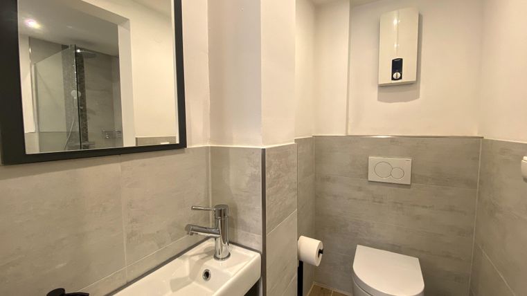 Een moderne badkamer met een elegante toilet en een klein wastafel. De muren zijn helder en vriendelijk betegeld.