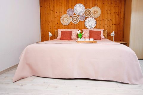 Een gezellige slaapkamer met een groot bed en een houten paneel. De muren zijn versierd met decoratieve manden en een kleine vaas met bloemen staat op het nachtkastje.