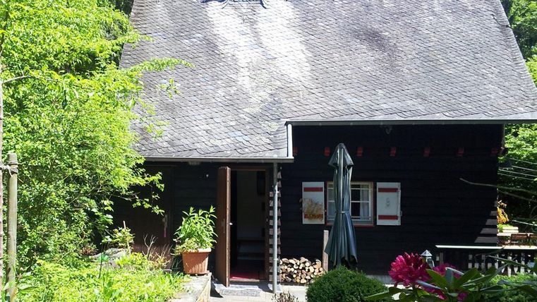 A charming wooden house surrounded by a green garden and trees. The front door is open and invites you into a cozy atmosphere.