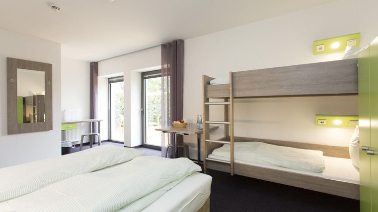 A modern room with a double bed and a bunk bed. Large windows provide plenty of daylight and a friendly atmosphere.