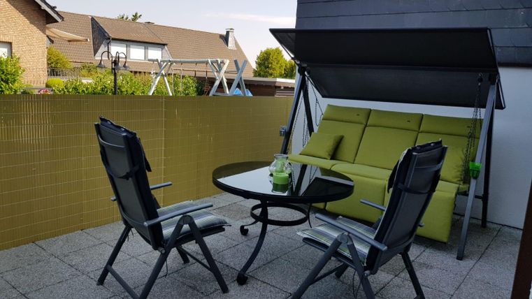 Ein gemütlicher Balkon mit einer grünen Schlafcouch und einem runden Tisch. Zwei Faltstühle stehen um den Tisch herum.
