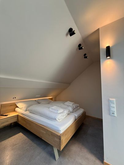 Een moderne slaapkamer met een houten bed en frisse bedlinnen. De muren zijn licht, en de verlichting is warm en uitnodigend.