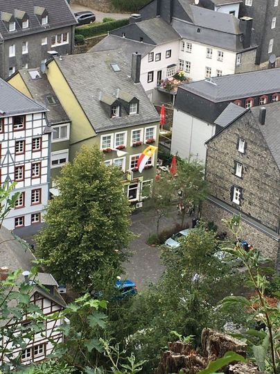 Een schilderachtig stadsgezicht met traditionele gebouwen en een groene boom op de voorgrond. Een vlag hangt aan een van de huizen en de straten zijn geplaveid.