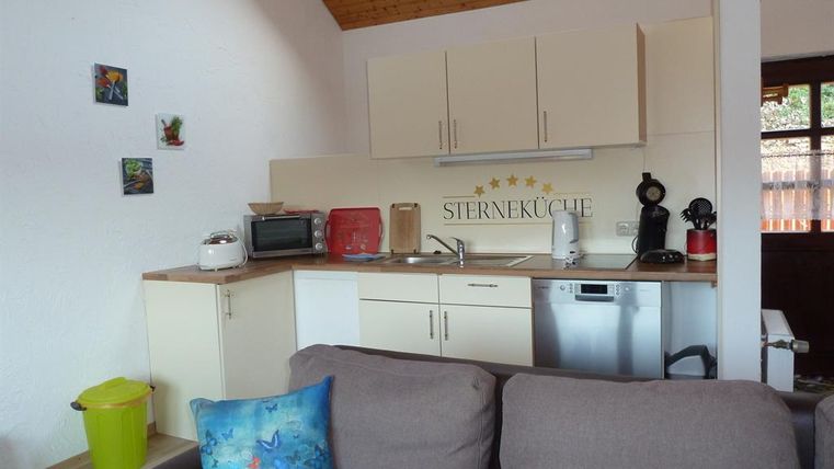 A modern kitchen interior with appliances and a cozy seating area. The walls are bright and decorated with small pictures.