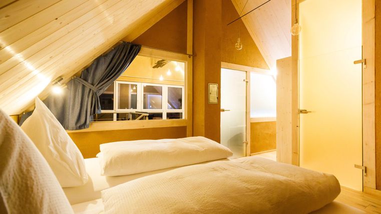 A cozy bedroom with sloping ceilings and wooden paneling. The room is bright and inviting, with a window and two white pillows.