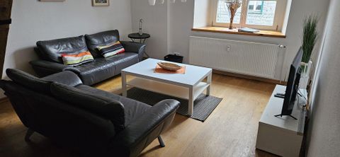 Een moderne woonkamer met twee zwarte banken en een witte salontafel. Op de tafel ligt een decoratie, en een televisie staat op een plank.