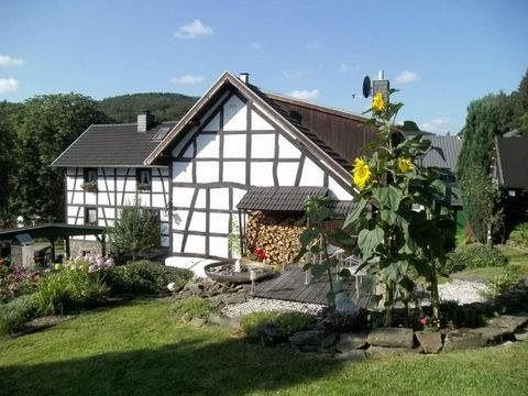 A charming half-timbered house surrounded by a beautiful garden. Sunflowers and well-maintained plants add color and life to the scene.