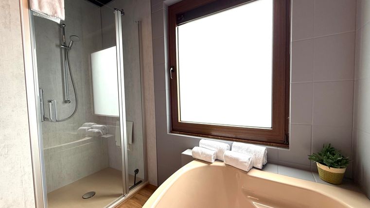 Een moderne badkamer met een douche en een badkuip. Het grote raam zorgt voor veel daglicht.