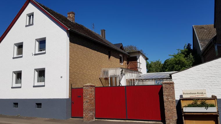 Een tweeledig huis met rode deuren en een witte gevel. De lucht is helder en blauw, en er is een klein tuingebied.