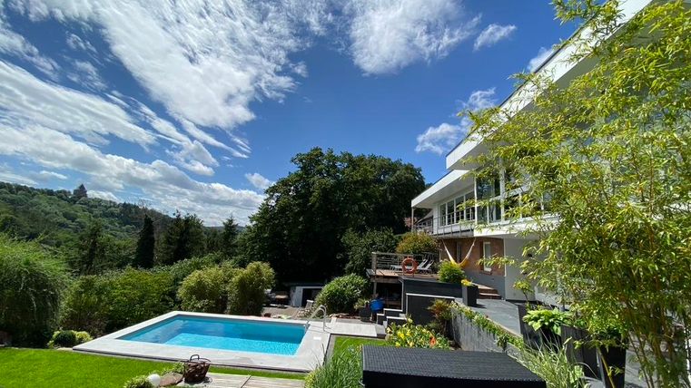 Een modern huis met een zwembad in de tuin. De lucht is helder en de omgeving is groen en uitnodigend.