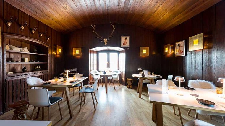 A cozy restaurant with dark wooden walls and a warm ambiance. Tables are elegantly set and equipped with modern chairs.