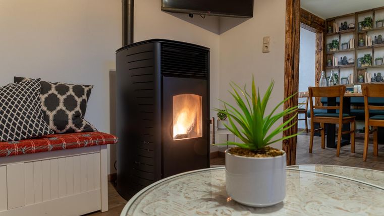 Een gezellige kamer met een moderne open haard die uitnodigende warmte uitstraalt. Op de tafel staat een plant in een witte pot, terwijl op de achtergrond een eettafel zichtbaar is.