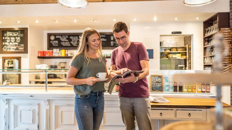 A couple is standing in a café and looking at a menu. They are holding cups in their hands and smiling.