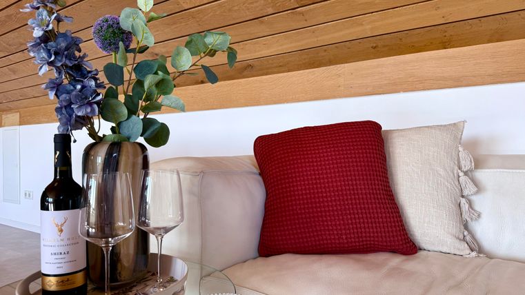 Een stijlvolle woonkamer met een bank, een rood kussen en een vaas met bloemen. Op de tafel staan een fles wijn en twee wijnglazen.