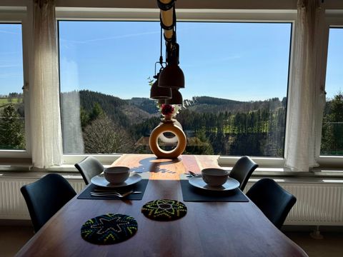 Een gezellige eetruimte met een houten tafel en twee kommen. Door het grote raam zie je een schilderachtig landschap met heuvels en bomen onder een heldere blauwe lucht.