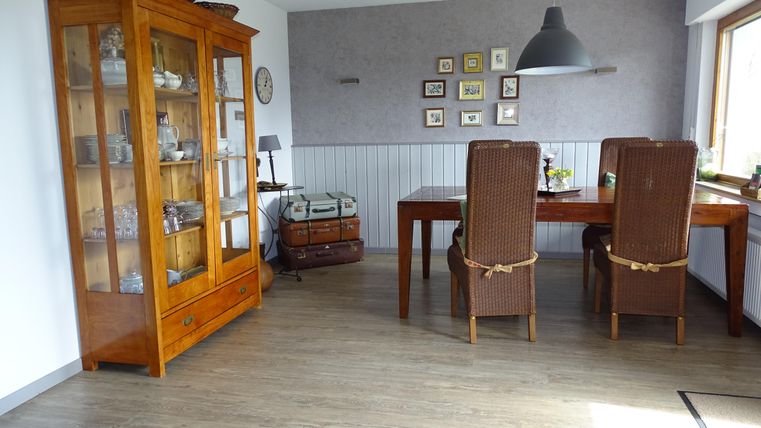 Een gezellige eetruimte met een houten kast en een grote tafel. De inrichting is licht en vriendelijk, met fotolijsten aan de muur.