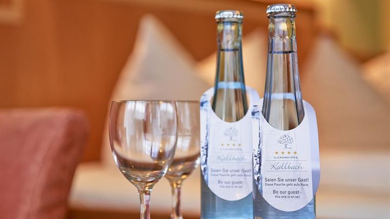 Zwei Flaschen stilles Wasser stehen neben zwei Gläsern auf einem Tisch. Im Hintergrund ist ein gemütliches Zimmerambiente sichtbar.