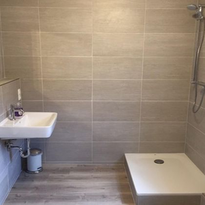 A modern bathroom with gray tiles and a walk-in shower. The sink and a mirror are also present.