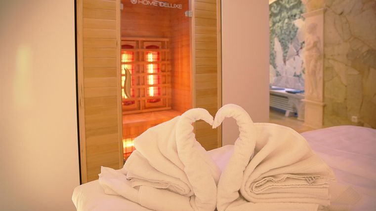 Een ontspannende wellnesskamer met twee handdoekvormige zwanen die een hart vormen. Op de achtergrond staat een infraroodsauna met warm licht.