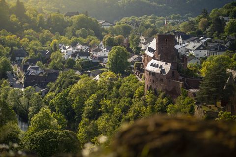 Een schilderachtig landschap met een kasteel en kleine, witte huizen. Omringd door groene bomen en zachte heuvels.