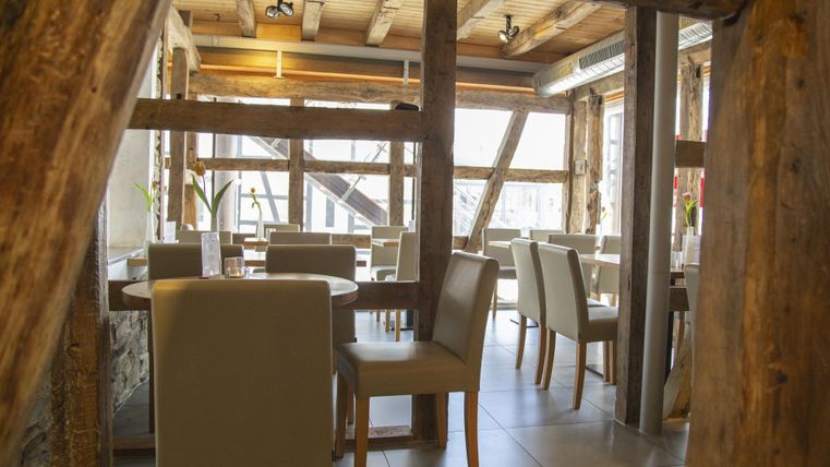 A cozy restaurant with wooden beams and elegant tables. The large window front provides plenty of light and an inviting atmosphere.